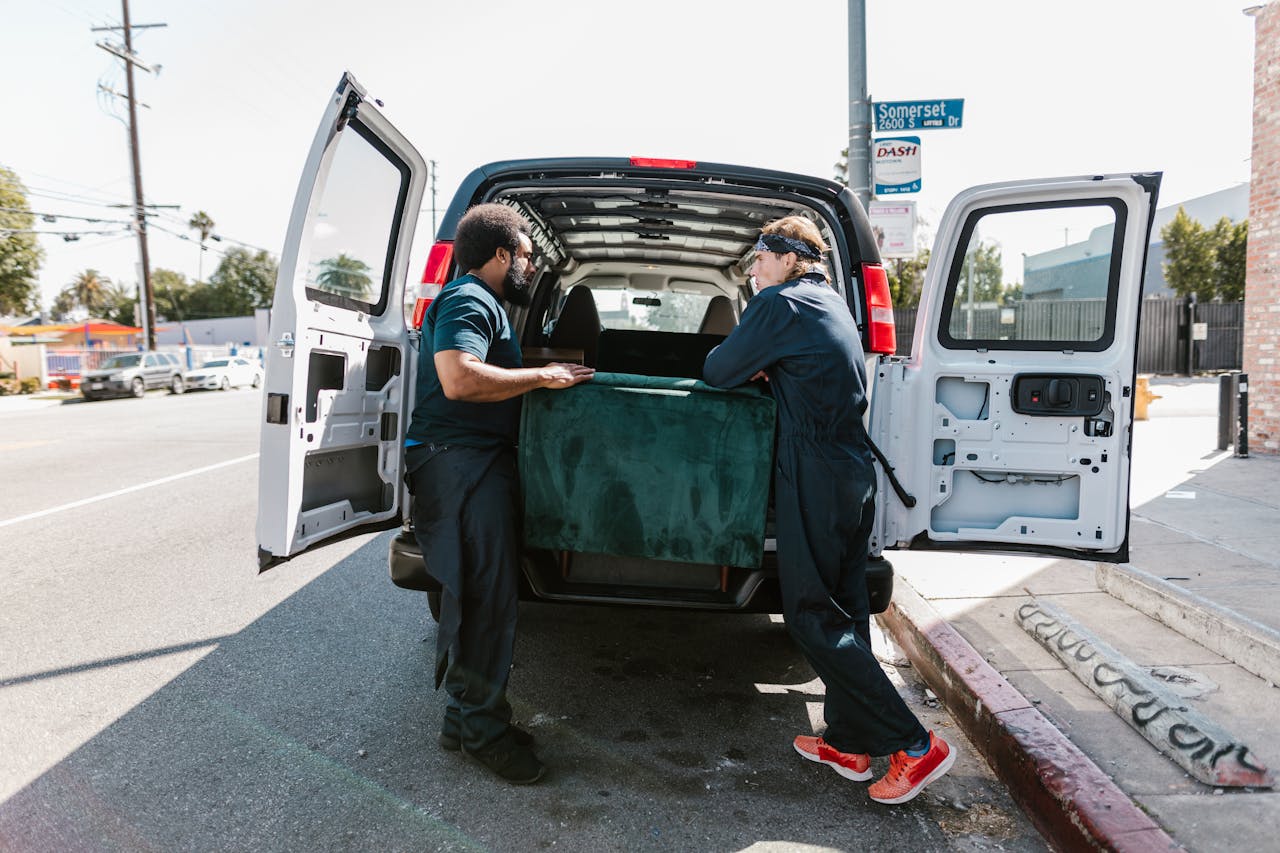 Two men loading a couch into a van on a sunny city street.